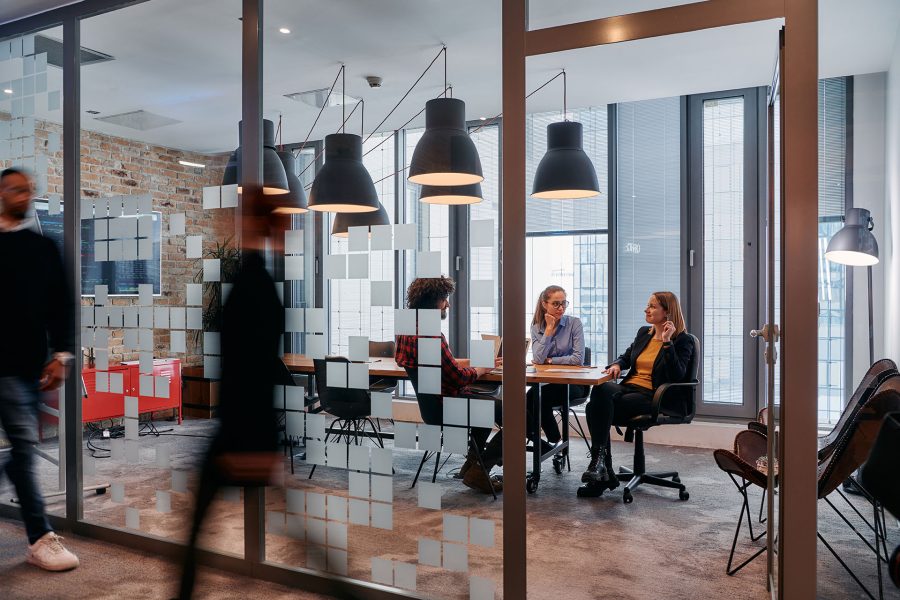 In the dynamic hustle and bustle of a business environment, a group of young business professionals walk down the corridor next to their office, while their colleagues collaborate inside, symbolizing teamwork and productivity.